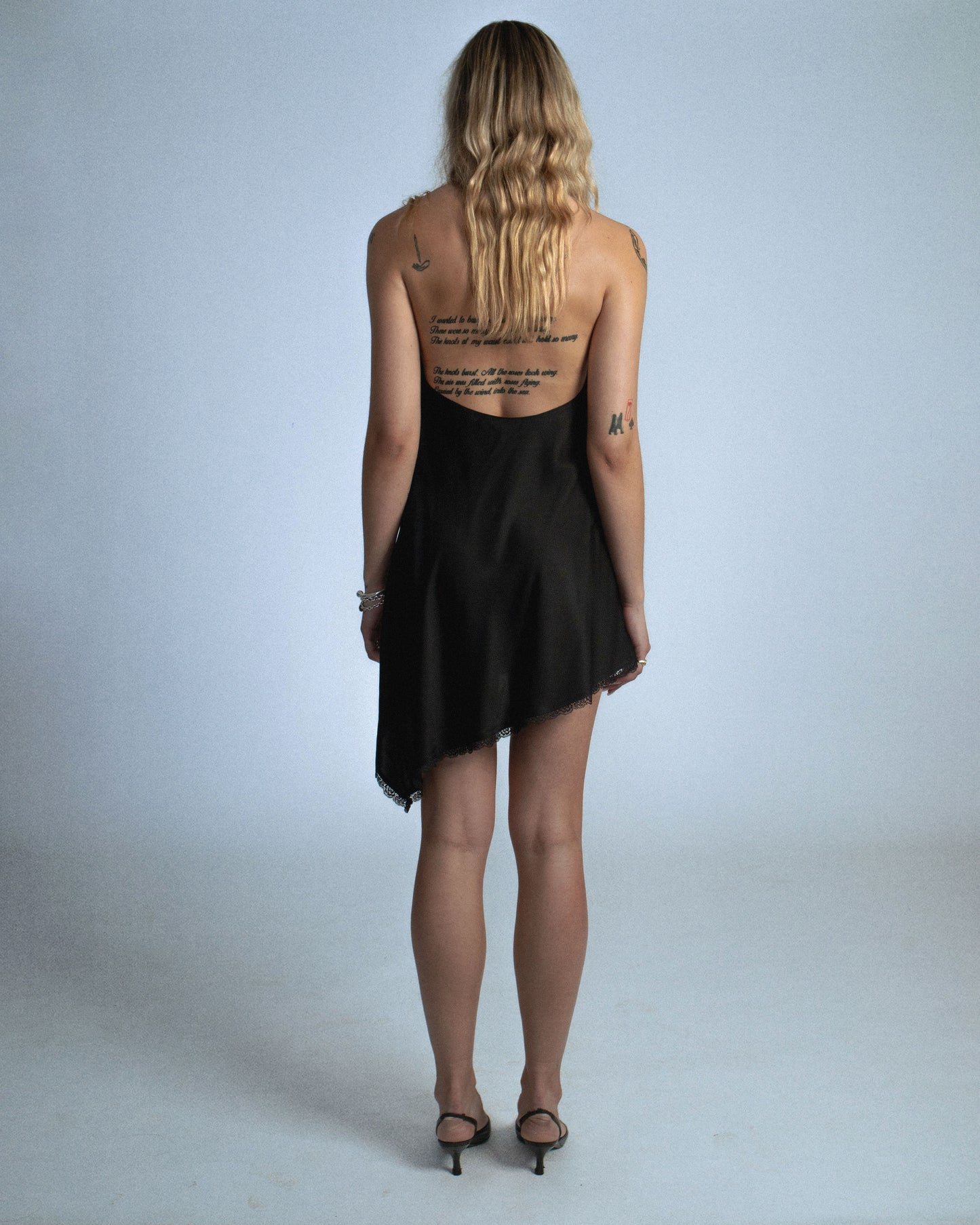 Silk cowl neck mini dress with distressed flower and silk/yarn trims hanging. Fabric is sewn on bias. Features silk buttons to conceal dress slit or cover for a more modest look. Comes with detachable silk snap belt. Deadstock trims from Japan. Perfect for elevated day-to-night looks. Shop now at Sivan Studio.