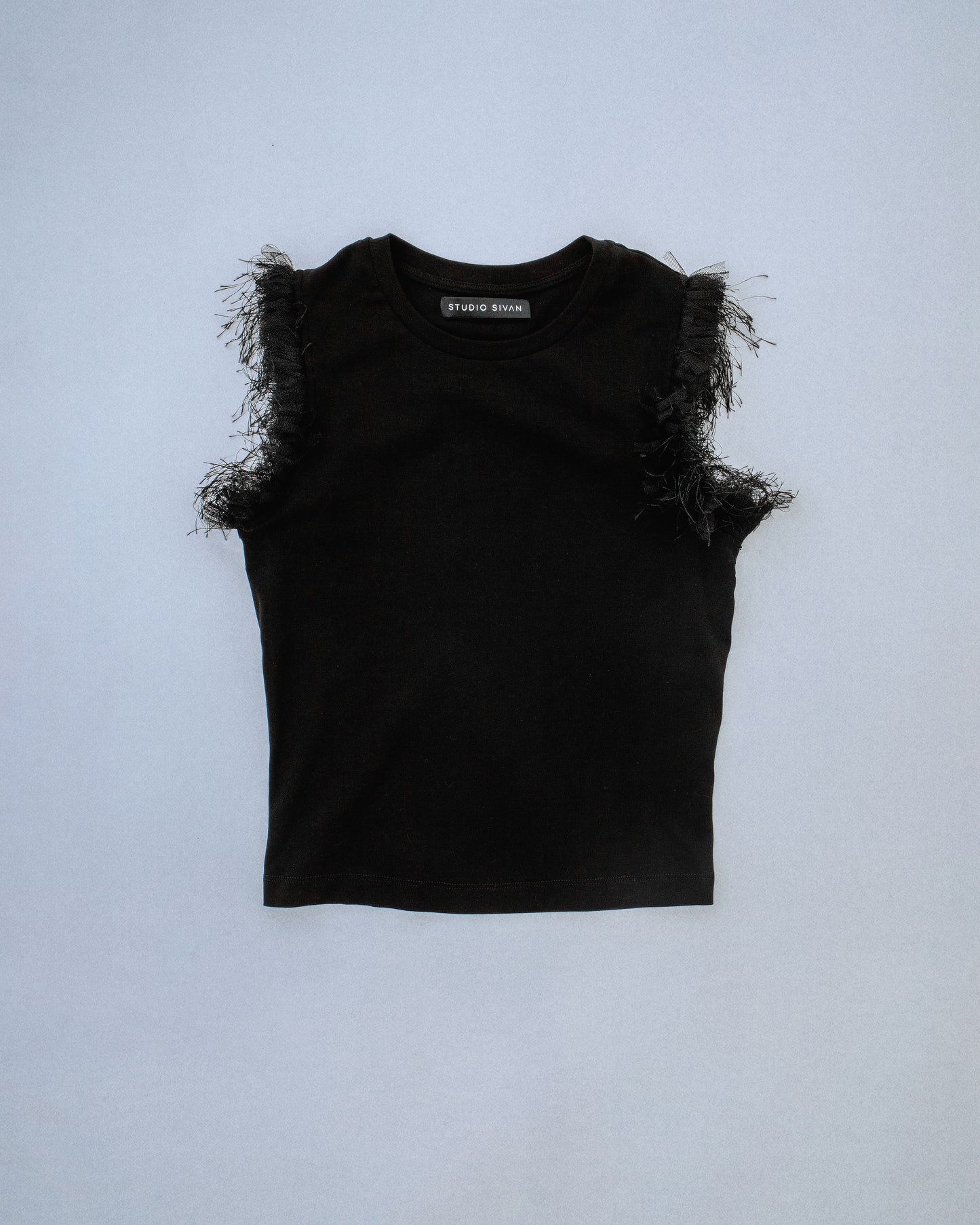 Fitted stretch cotton tank with layered trim made of lace, tulle, and distressed eyelash fringe along the sleeve opening. Adds an undone, tactile detail to a clean silhouette. Perfect for elevated day-to-night looks. Shop now at Sivan Studio.
