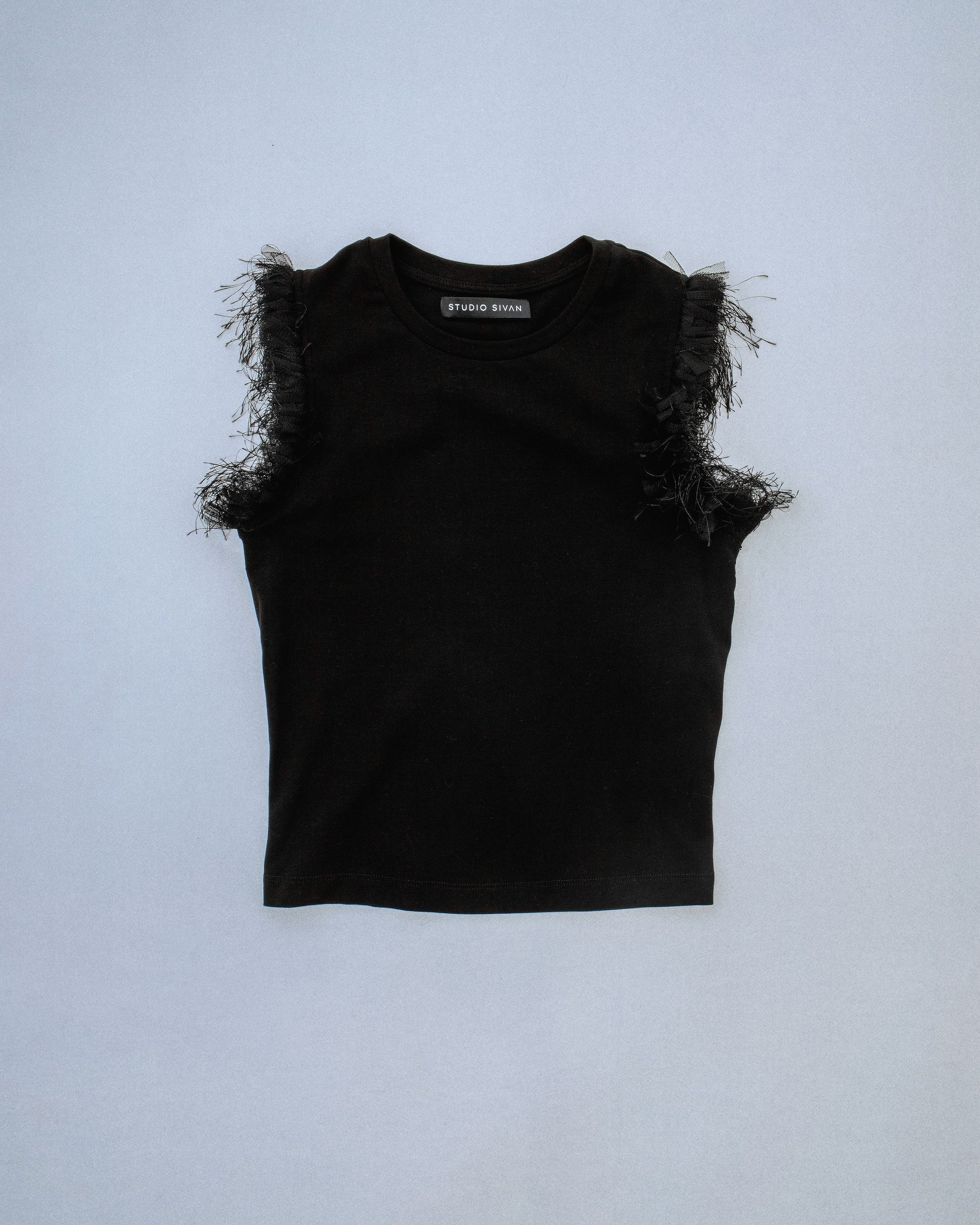 Fitted stretch cotton tank with layered trim made of lace, tulle, and distressed eyelash fringe along the sleeve opening. Adds an undone, tactile detail to a clean silhouette. Perfect for elevated day-to-night looks. Shop now at Sivan Studio.