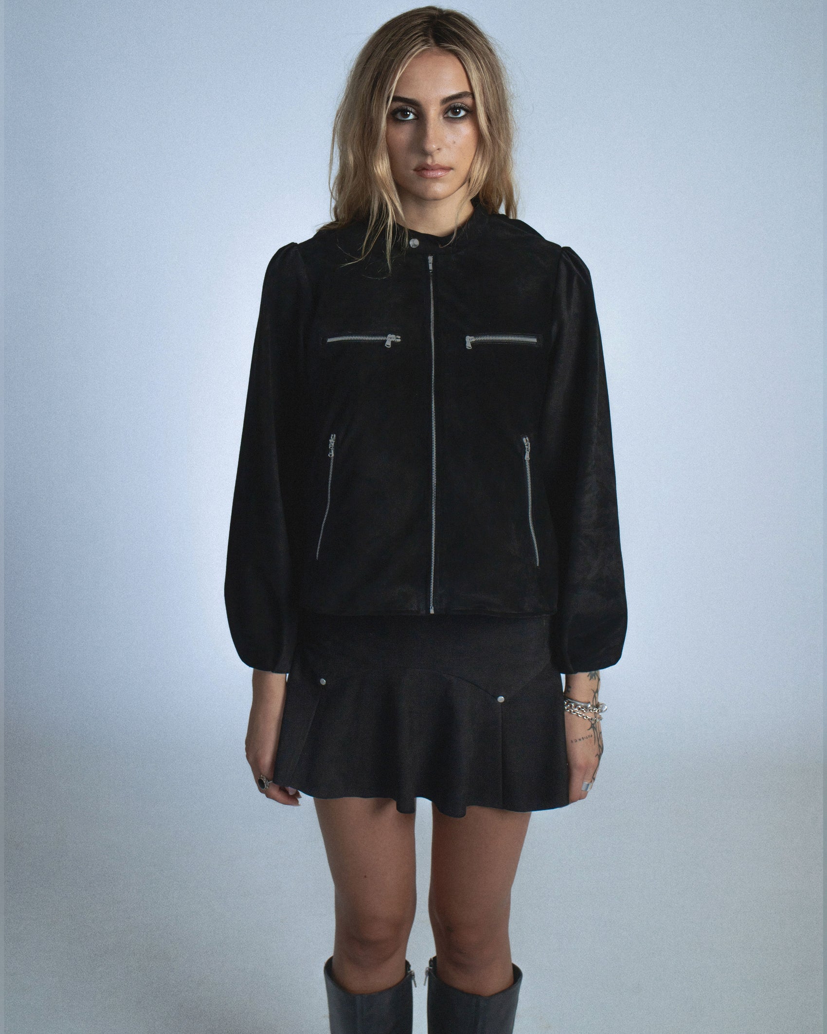 Suede jacket with exposed gunmetal zippers and soft balloon sleeves. The back features structured, sewn-down panel pleats running down the center for a sculptural spine like effect. Perfect for elevated day-to-night looks. Shop now at Sivan Studio.