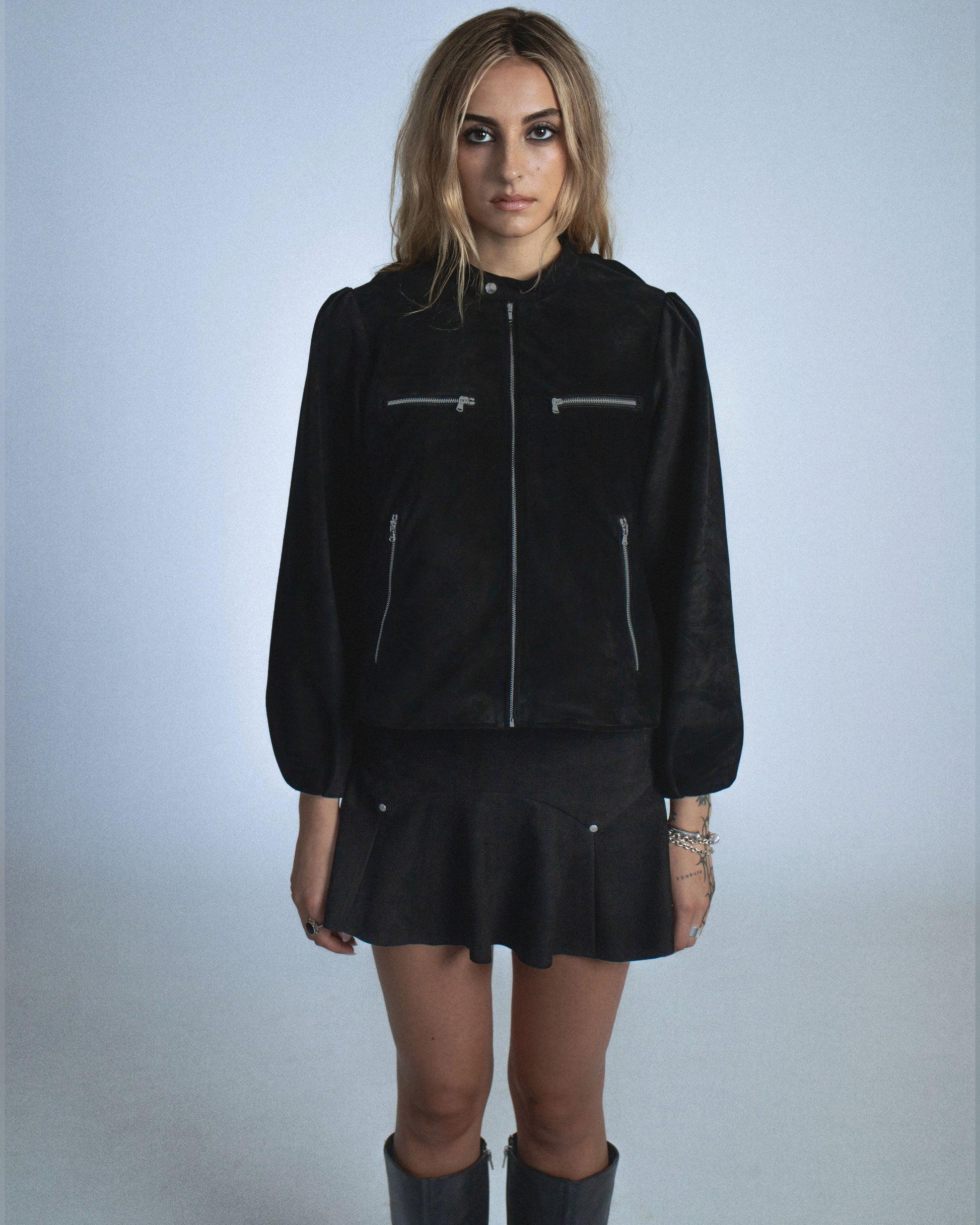 Suede jacket with exposed gunmetal zippers and soft balloon sleeves. The back features structured, sewn-down panel pleats running down the center for a sculptural spine like effect. Perfect for elevated day-to-night looks. Shop now at Sivan Studio.