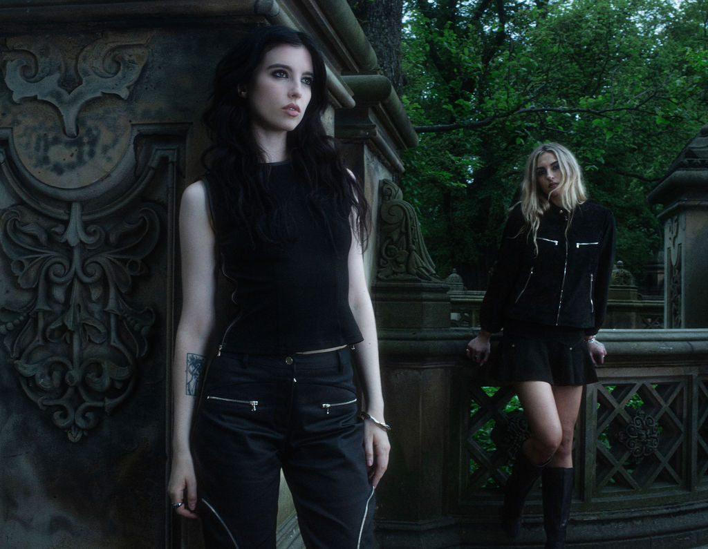 Two women in dark clothing standing in a gothic-style setting with ornate architecture.