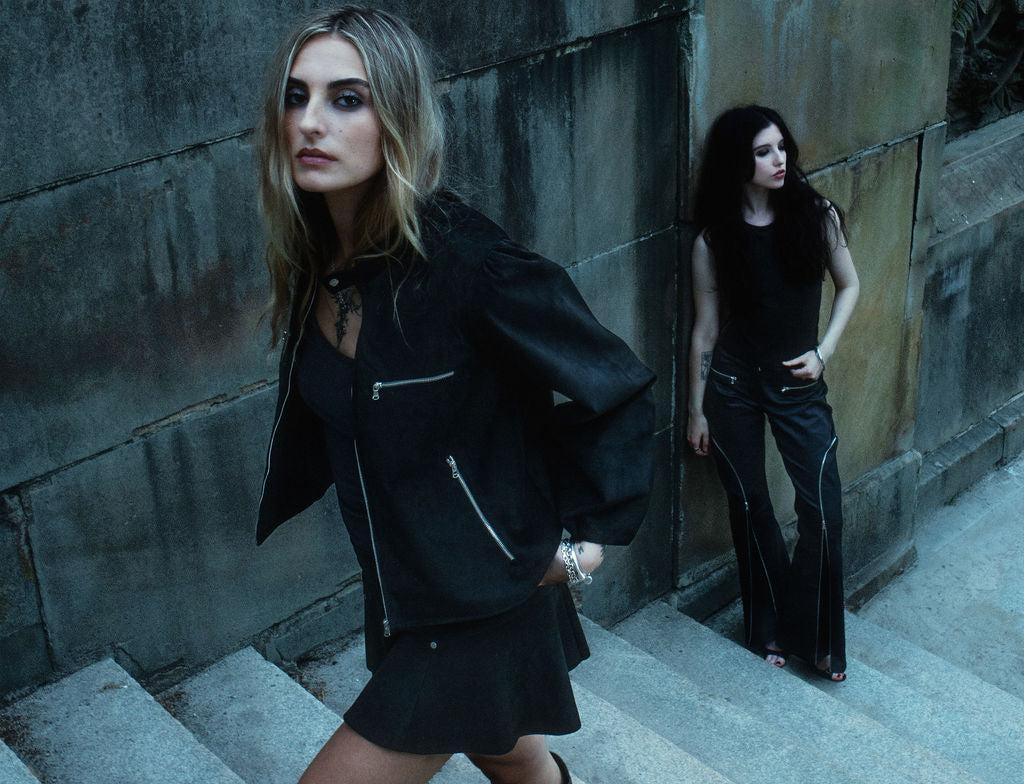Two women in dark clothing standing on a staircase against a textured wall.