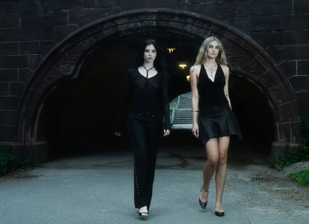 Two women in black outfits walking out of a dark tunnel.
