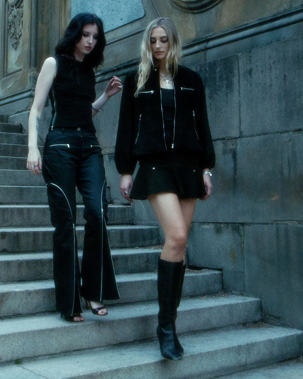 Two women in black outfits standing on stone steps.