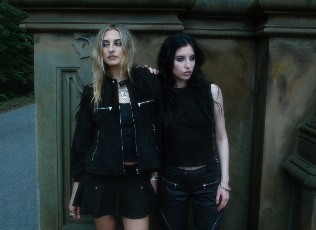 Two women in black outfits standing against a textured wall.