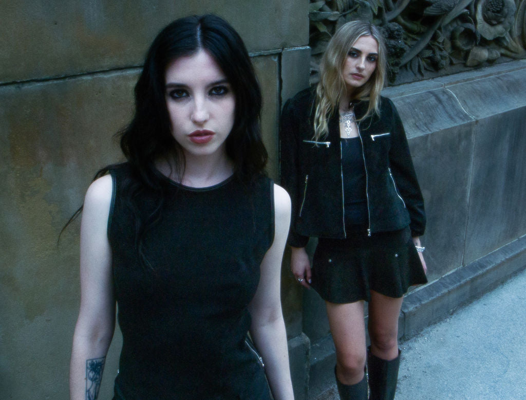 Two women in dark clothing standing against a textured wall.
