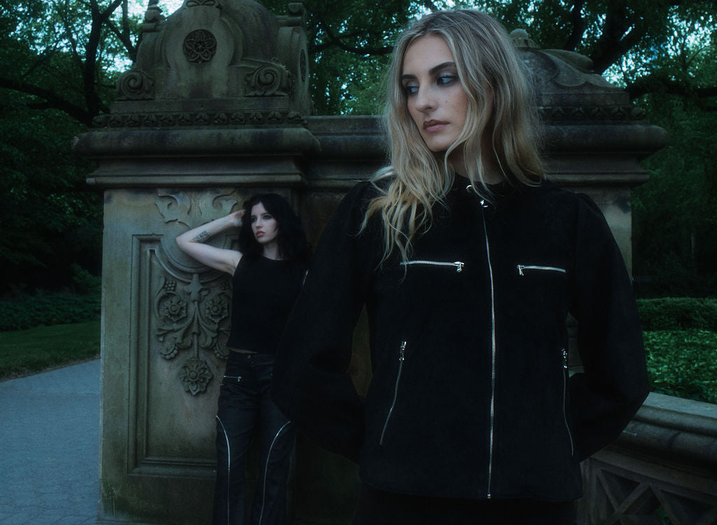 Two women in dark clothing standing in a park with ornate stone structures.
