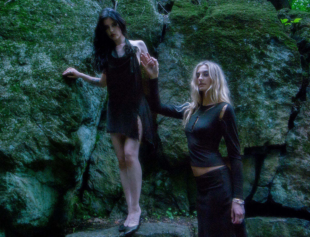 Two women in black outfits standing against a rocky background