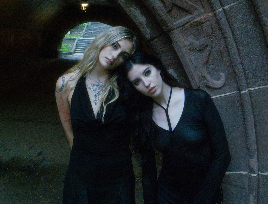Two women in black dresses standing against a stone wall.