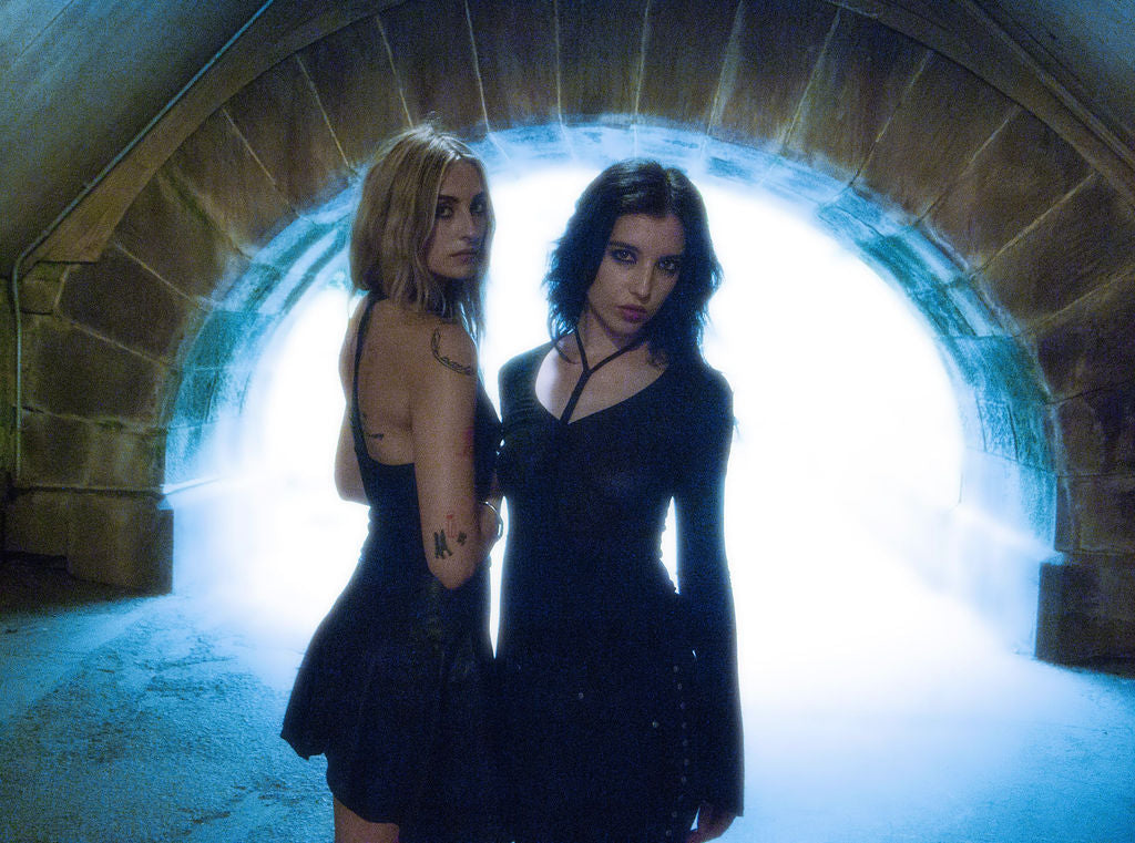Two women in black dresses standing in a tunnel with a bright light at the end.