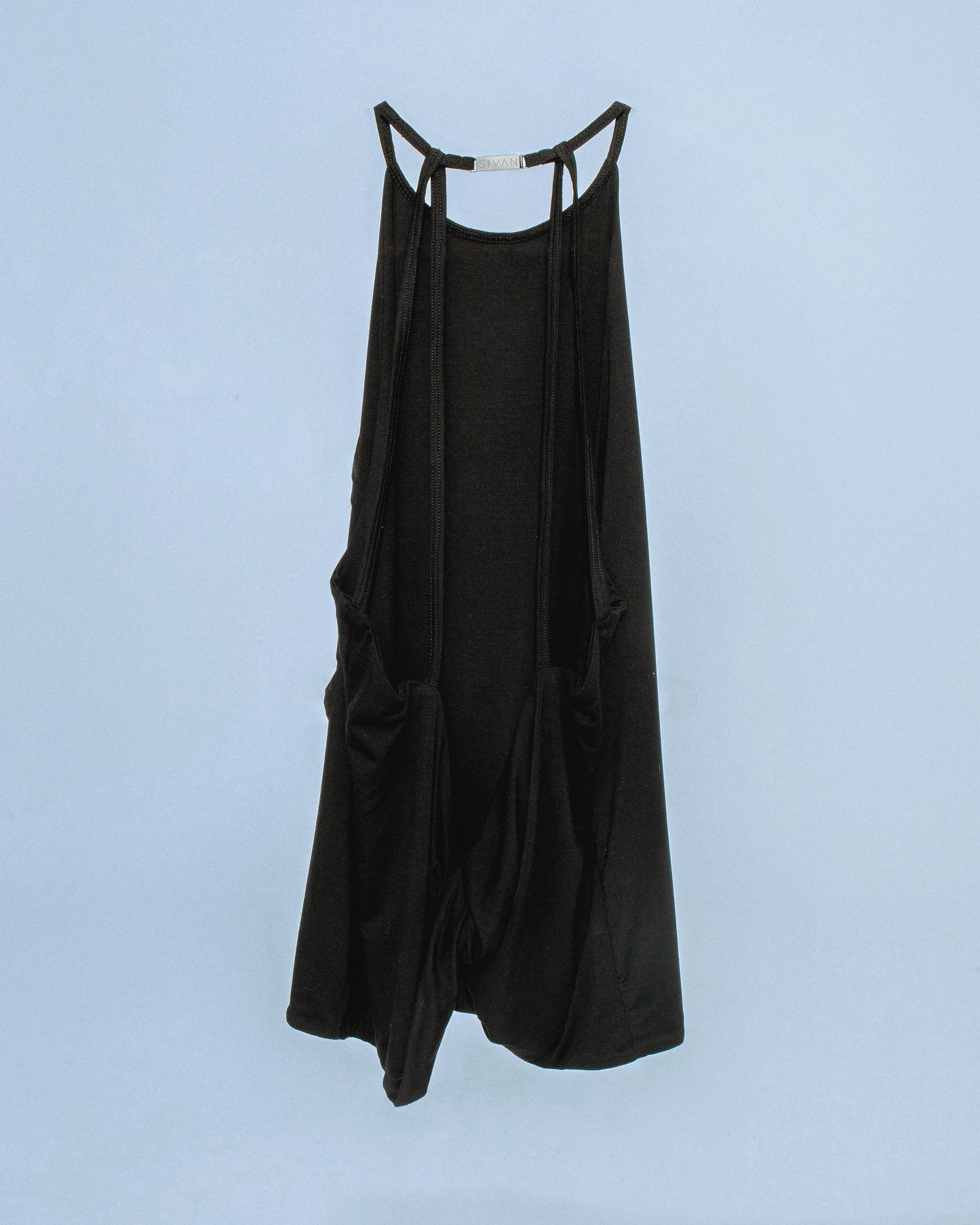 Halter neck top with a soft, fluid drape and open back. Twisted at the lower back with delicate strap detailing. Secured with an engraved gunmetal logo clasp at the neck. Available in black and white. Black top features gunmetal clasp. Perfect for elevated day-to-night looks. Shop now at Sivan Studio.