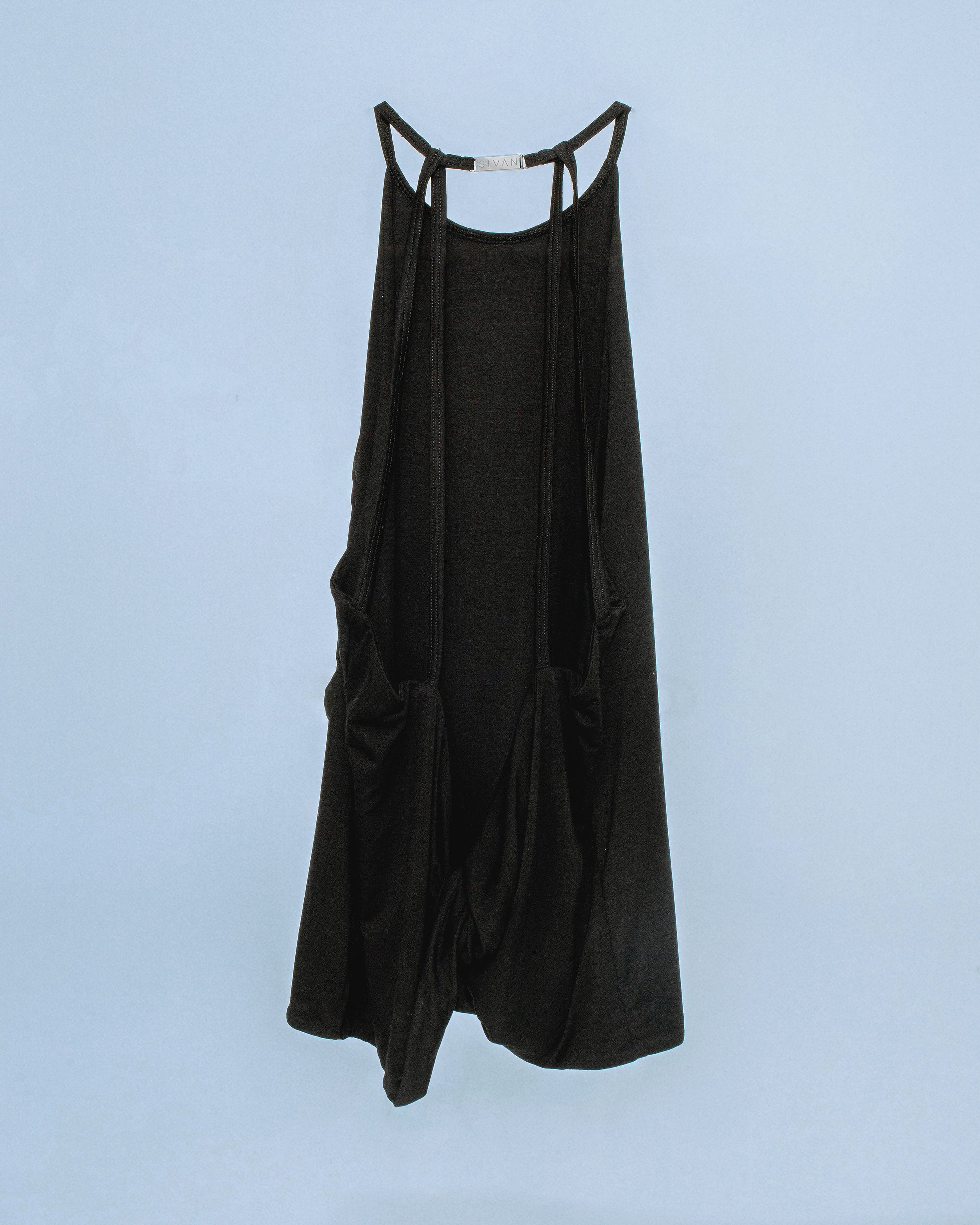 Halter neck top with a soft, fluid drape and open back. Twisted at the lower back with delicate strap detailing. Secured with an engraved gunmetal logo clasp at the neck. Available in black and white. Black top features gunmetal clasp. Perfect for elevated day-to-night looks. Shop now at Sivan Studio.