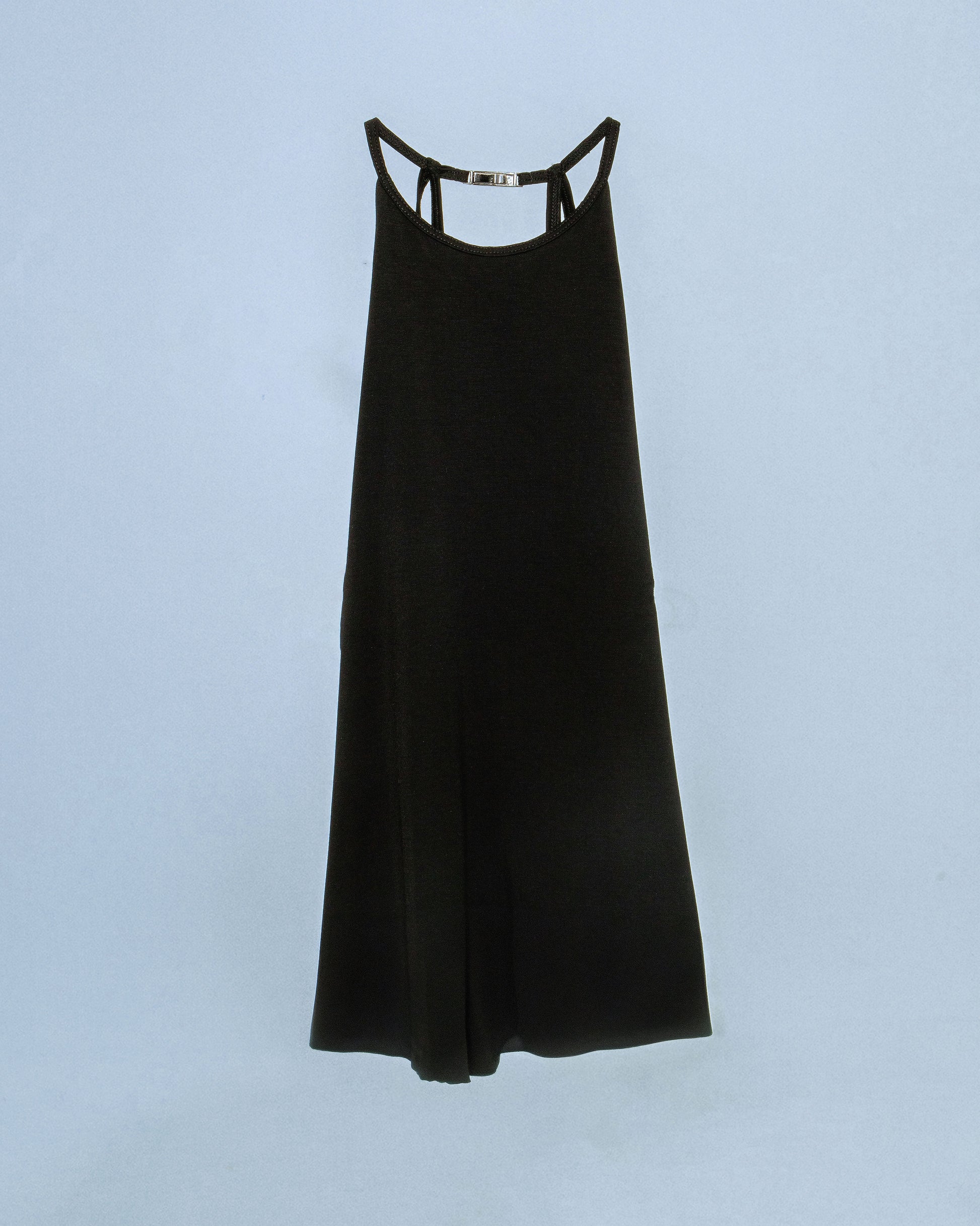 Halter neck top with a soft, fluid drape and open back. Twisted at the lower back with delicate strap detailing. Secured with an engraved gunmetal logo clasp at the neck. Available in black and white. Black top features gunmetal clasp. Perfect for elevated day-to-night looks. Shop now at Sivan Studio.