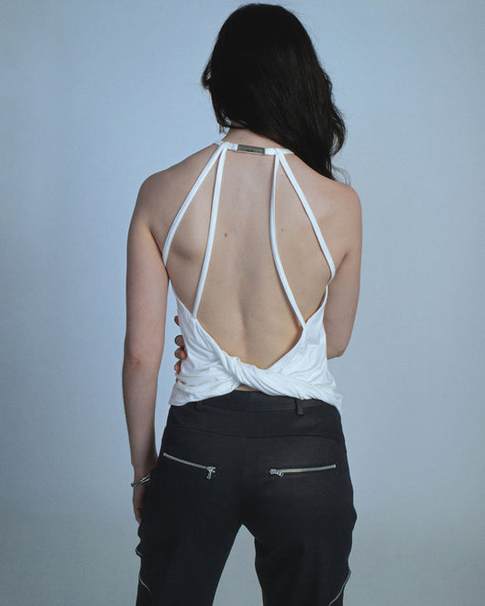 Halter neck top with a soft, fluid drape and open back. Twisted at the lower back with delicate strap detailing. Secured with an engraved silver studio Sivan logo clasp at the neck that clicks to open. Available in black and white. Black top features gunmetal clasp. Perfect for elevated day-to-night looks. Shop now at Sivan Studio.