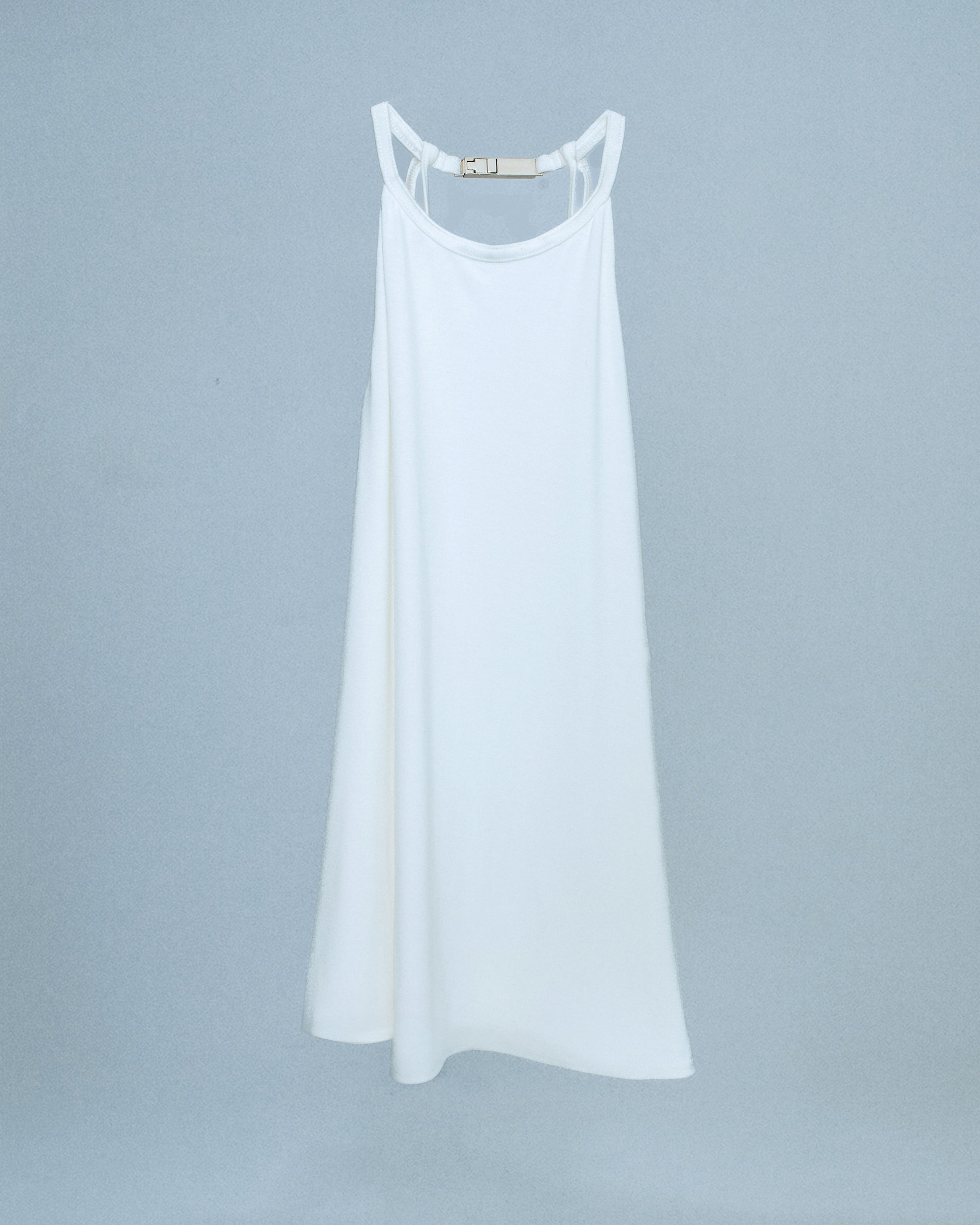 Halter neck top with a soft, fluid drape and open back. Twisted at the lower back with delicate strap detailing. Secured with an engraved silver studio Sivan logo clasp at the neck that clicks to open. Available in black and white. Black top features gunmetal clasp. Perfect for elevated day-to-night looks. Shop now at Sivan Studio.