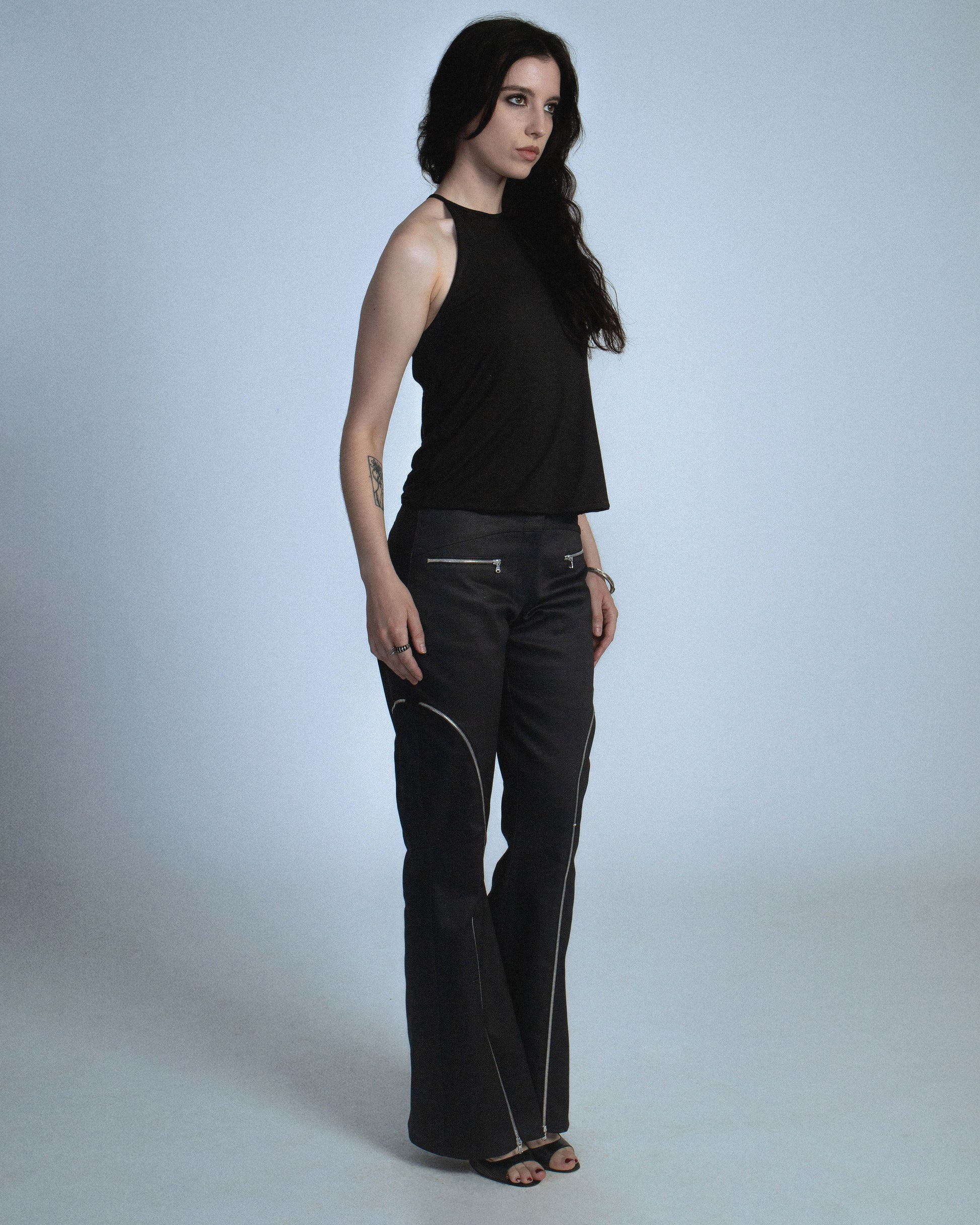 Halter neck top with a soft, fluid drape and open back. Twisted at the lower back with delicate strap detailing. Secured with an engraved gunmetal logo clasp at the neck. Available in black and white. Black top features gunmetal clasp. Perfect for elevated day-to-night looks. Shop now at Sivan Studio.