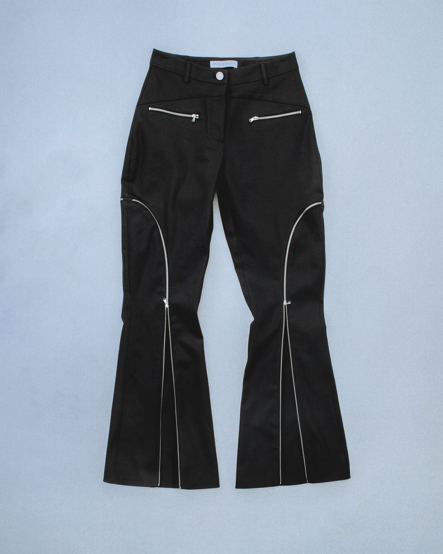 Flared waxed stretch denim zipper pant.  Zipper opens up until knee to flare pant leg even more. Features exposed front and back silver zippers. Custom laser engraved button hardware. Perfect for elevated day-to-night looks. Shop now at Sivan Studio.